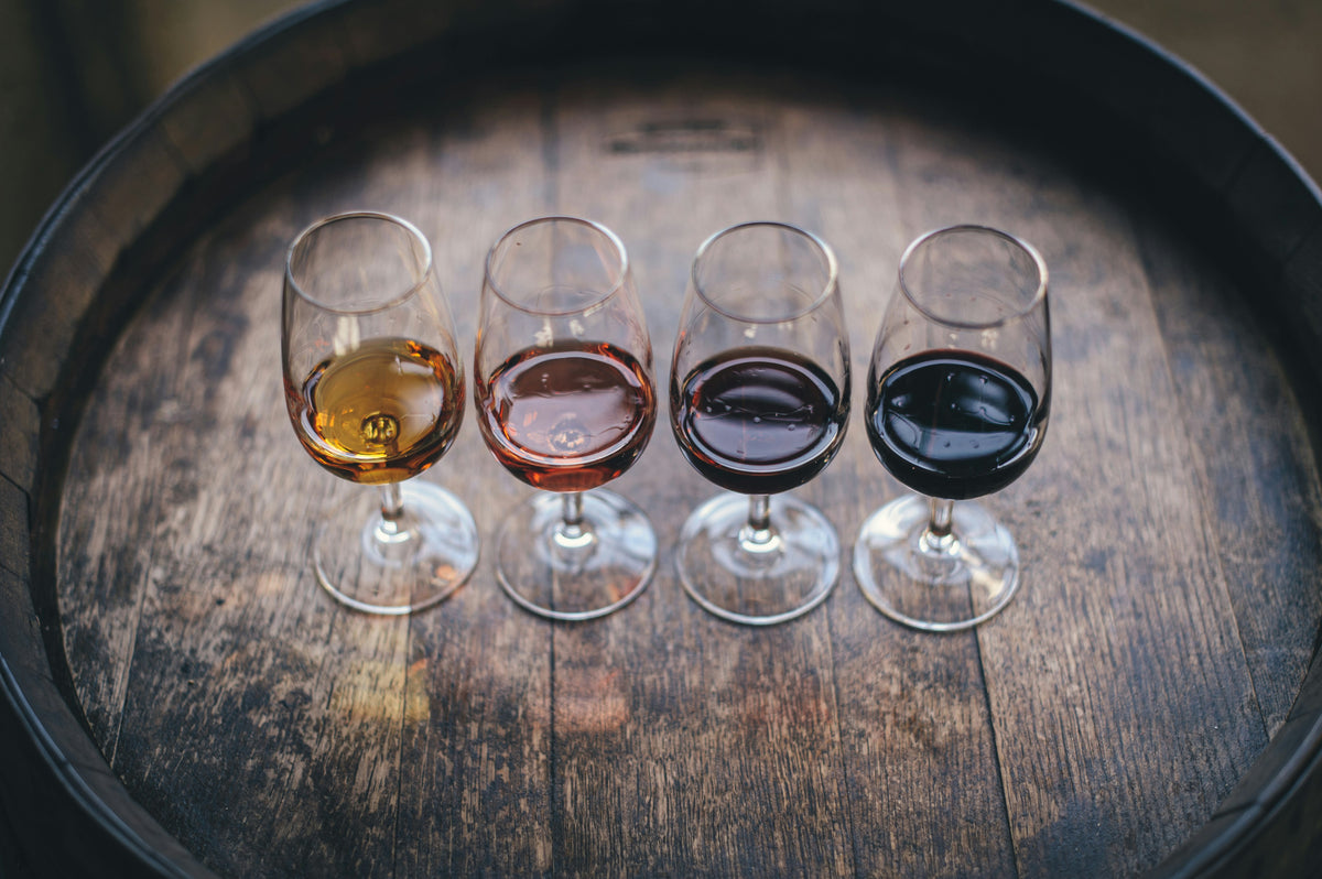 Four wine glasses with different colored wines on a wooden barrel