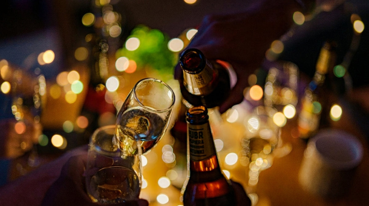 A celebratory toast with champagne glasses and beer bottles, set against a glowing, blurred festive light background.